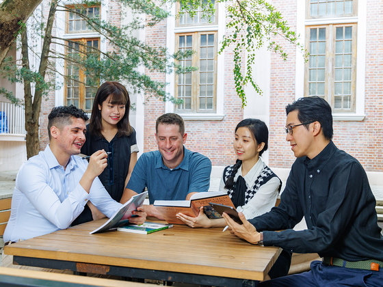 Students studying together at an outdoor table near a brick building.