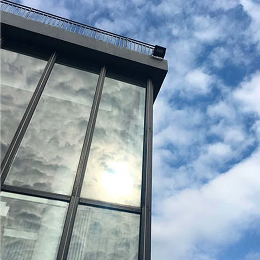 Low-angle view of a modern glass building under a bright, cloud-dappled sky.