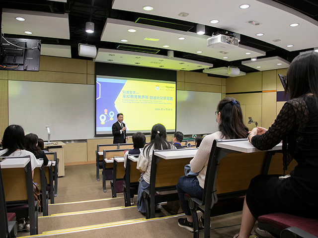 A speaker presents in a lecture hall with attendees seated